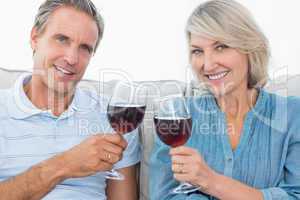 Couple toasting with red wine on the sofa smiling at camera