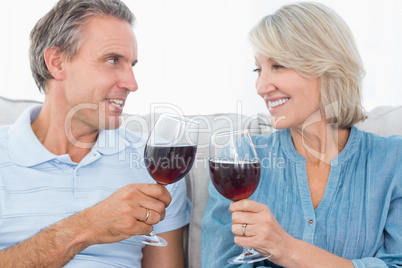 Couple toasting each other with red wine on the sofa