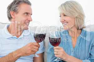 Couple toasting each other with red wine on the sofa