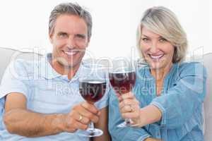Couple toasting to the camera with red wine on the sofa