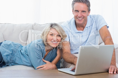 Happy couple using their laptop looking at camera