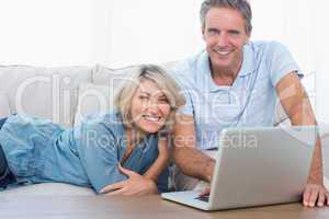 Happy couple using their laptop looking at camera