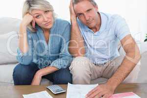 Anxious couple going over bills looking at camera