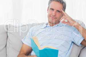 Man relaxing on his couch with a book looking at camera