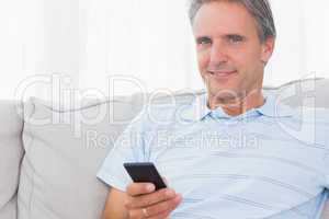Man relaxing on his couch sending a text smiling at camera