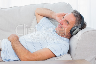 Man lying on couch listening to music smiling at camera