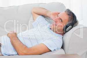 Man lying on couch listening to music smiling at camera
