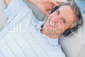 Man lying on sofa listening to music smiling at camera