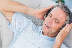 Man lying on sofa listening to music with eyes closed