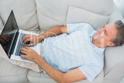 Man lying on couch typing on laptop