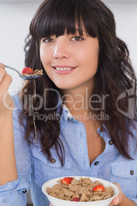Smiling brunette having bowl of cereal and fruit