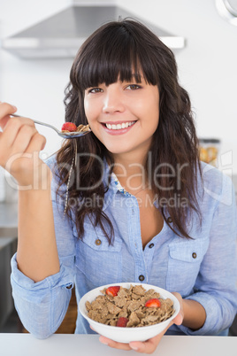 Happy brunette eating bowl of cereal and fruit