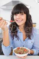 Happy brunette eating bowl of cereal and fruit