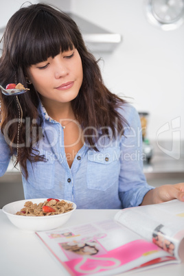 Pretty brunette eating cereal and reading magazine