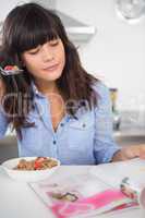 Pretty brunette eating cereal and reading magazine