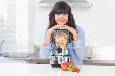 Pretty brunette leaning on her juicer full of fruit