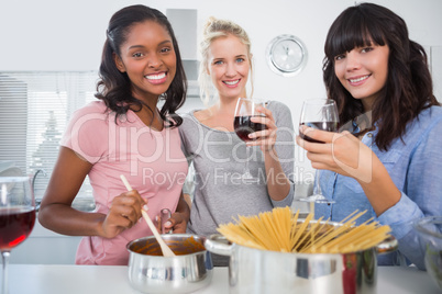 Cheerful friends making spaghetti dinner together and drinking r