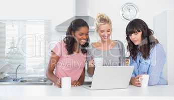 Smiling friends having coffee together and looking at laptop