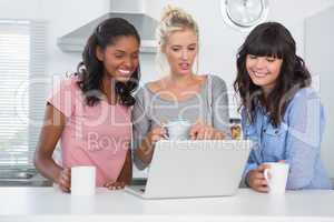 Happy friends having coffee together and looking at laptop