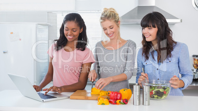 Happy friends making salad and using laptop for recipe
