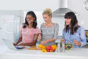 Smiling friends making salad and using laptop for recipe