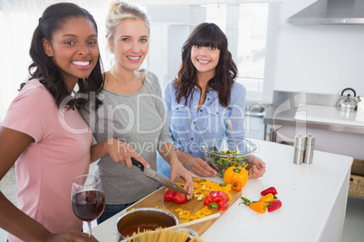 Cheerful friends preparing a meal together looking at camera