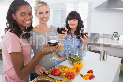 Cheerful friends preparing a meal together and drinking red wine