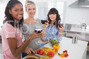 Cheerful friends preparing a meal together and drinking red wine