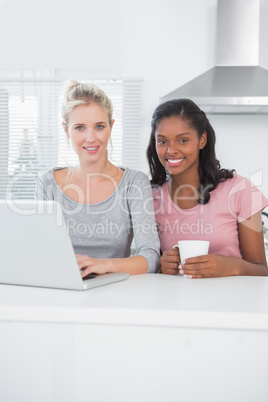 Pretty friends using laptop together and smiling at camera