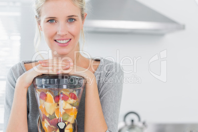 Blonde woman leaning on her juicer and smiling at camera