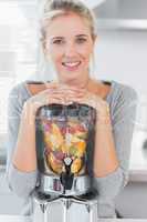 Blonde woman leaning on her juicer full of fruit and smiling at
