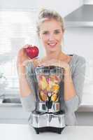 Pretty woman leaning on her juicer full of fruit and holding red