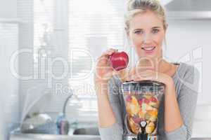 Happy woman leaning on her juicer full of fruit and holding red