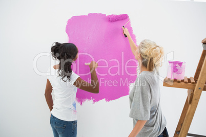 Happy young housemates painting wall pink
