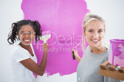 Cheerful young housemates painting wall pink