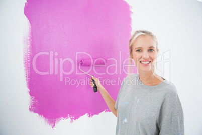 Smiling blonde painting her wall pink
