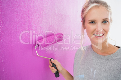 Cheerful blonde painting her wall pink