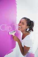 Laughing young woman painting her wall in pink