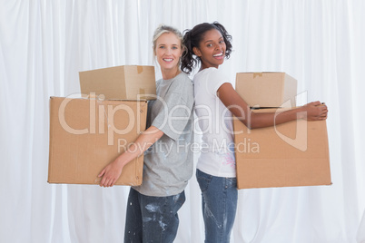 Happy friends standing back to back holding moving boxes