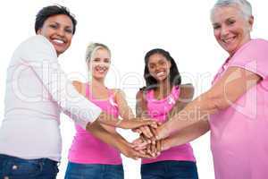 Smiling women wearing breast cancer ribbons putting hands togeth