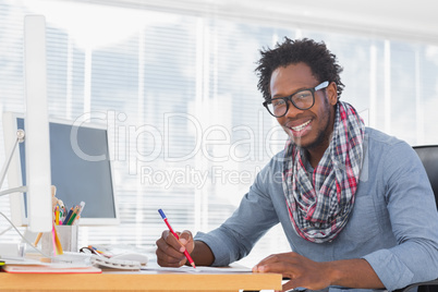 Smiling designer drawing with a red pencil on a desk