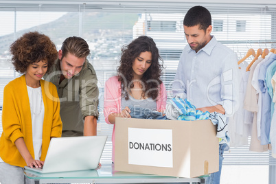 Volunteers using a laptop and taking clothes from charity box