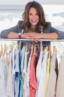 Smiling fashion designer leaning on clothes