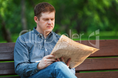 man reads newspaper on bench in the park