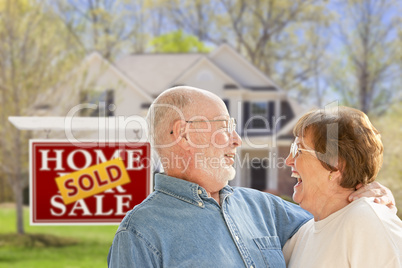 Senior Couple in Front of Sold Real Estate Sign and House