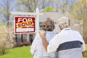 Senior Couple in Front of Sold Real Estate Sign and House