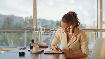 young, beautiful girl sits at a table and writes the entries in the notebook