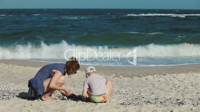 young mother with her son play in the sand at the beach. They collect shells