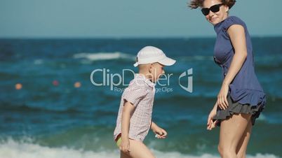 young mother with her son play in the sand at the beach. They collect shells