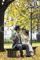 Old-fashioned dressed couple on a park bench in fall.